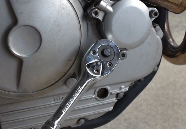 ヤマハのオフロードバイクのセロー250のエンジンにあるオイル注入口のボルトをソケットレンチで緩める様子